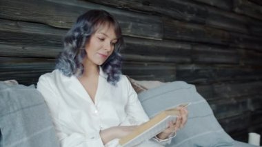 Yatakta pijama giymiş kitap okuyan güzel genç bir bayanın ağır çekimde