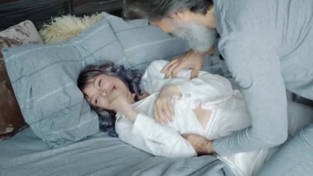 Joyful marido cócegas bonito jovem esposa se divertindo com a mulher, em seguida, beijando na cama em casa — Vídeo de Stock