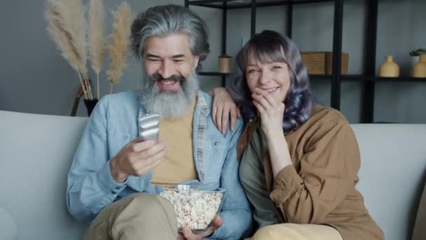 Portrait of couple watching TV and eat popcorn looking and pointing at screen at home — Stok Video
