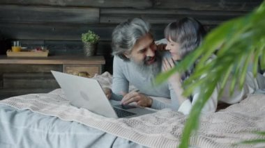 Kadın ve erkek pijama giyiyor dizüstü bilgisayar kullanıyor ve yatak odasında sohbet ediyor.