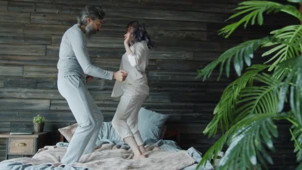 Movimento lento de homem e mulher vestindo pijama dançando e rindo na cama em casa — Vídeo de Stock