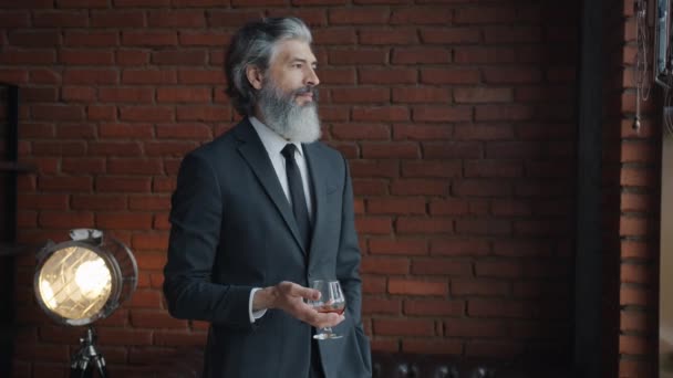 Slow motion portrait of attractive mature businessman standing with glass of cognac in office smiling — Stock Video