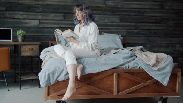 Elegante giovane donna lettura libro seduto a letto a casa rilassante nel tempo libero — Video Stock