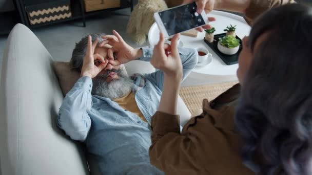 Joyful volwassen man poseren voor smartphone camera terwijl vrouw het nemen van foto 's aanraken scherm — Stockvideo