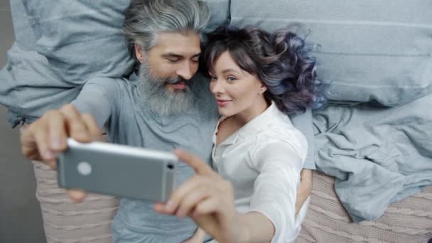Vousatý muž přičemž selfie v posteli s krásnou manželkou pomocí smartphone kamery baví — Stock video