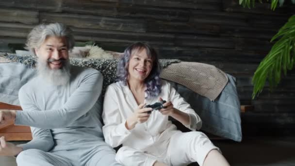 Mann und Frau im Pyjama spielen Videospiel im Schlafzimmer zu Hause und haben Spaß zusammen — Stockvideo