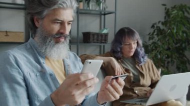 Olgun bir adamın internetten alışveriş yapması, banka kartıyla ödeme yapması, karısının da onaylamaması için başını sallaması.