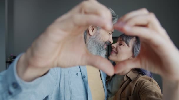 Retrato en cámara lenta del hombre y la mujer sonriendo mirando a la cámara haciendo forma de corazón con las manos — Vídeos de Stock