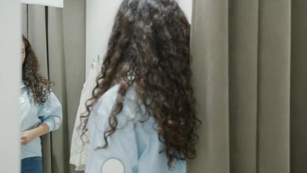 Roztomilé mladé brunetky se snaží na nové tričko v šatně při pohledu na zrcadlo s úsměvem — Stock video