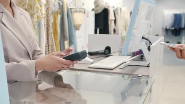 Close-up af kvindelige kunde at foretage betaling med smartphone i tøj butik tager tasker – Stock-video