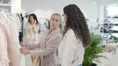 Kıyafet alışverişi yapan mutlu kızlar şık kıyafetler seçip butikte sohbet ediyorlar.