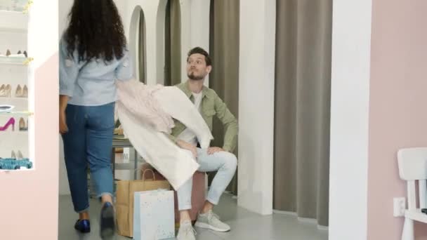 Glada make väntar på fru nära passande rum i kläder butik sedan leende välja klänningar — Stockvideo