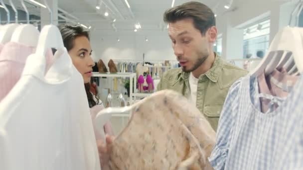 Ongelukkig echtpaar vechten in de winkel kiezen kleding schreeuwen en gebaren houden kleding — Stockvideo