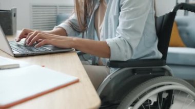 Bilgisayarlı daktilo kullanan tanınmayan engelli bir kız online işlerle meşgul tekerlekli sandalyede oturuyor.