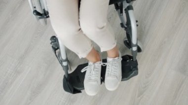 Tekerlekli sandalyede oturan belden aşağısı felçli kadının yüksek açılı görüntüsü.