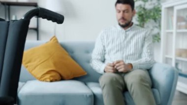 Depresyondaki engelli bir adamın tek başına koltukta oturup tekerlekli sandalyeye bakarak ağlaması.