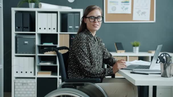 Retrato de alegre jovem senhora em cadeira de rodas sorrindo olhando para a câmera dentro de casa no escritório — Vídeo de Stock