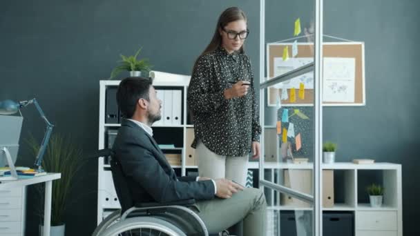 坐在轮椅上的年轻女子和残疾男子在办公室的玻璃板上写着便条 — 图库视频影像
