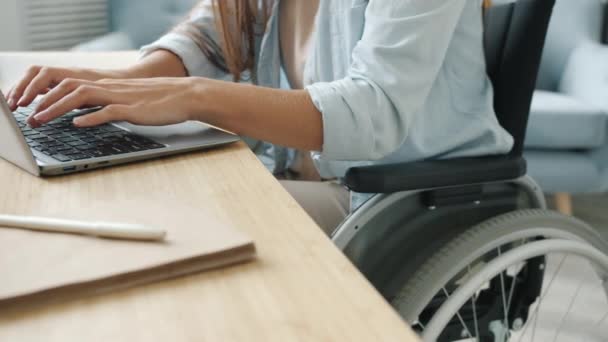 Cámara lenta de la estudiante que aprende en línea usando el ordenador portátil que mecanografía que se sienta en silla de ruedas en apartamento — Vídeos de Stock