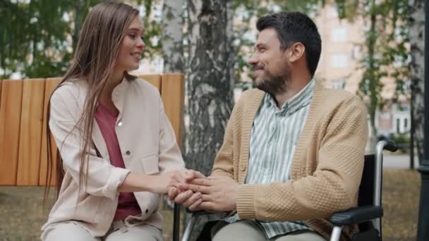 Lykkelige par handicappede fyr og flot pige taler holder hænder i byparken – Stock-video