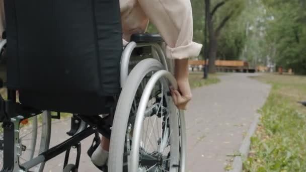 Close-up câmera lenta de mulher com deficiência montando cadeira de rodas ao ar livre no parque — Vídeo de Stock