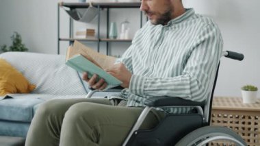 Evde tekerlekli sandalyede oturup kitap okuyan engelli yakışıklı adamın portresi.