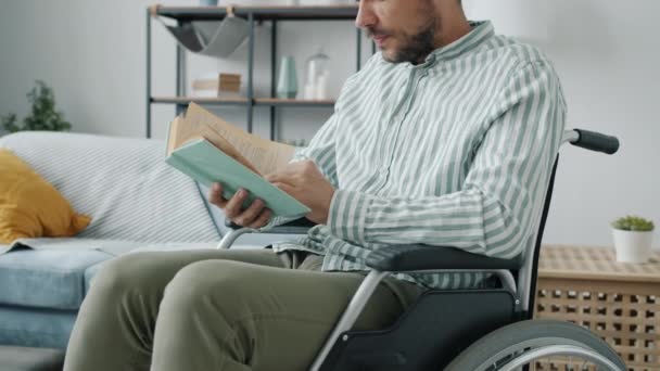 Portrait of handsome disabled man reading book sitting in wheelchair at home — Stock Video