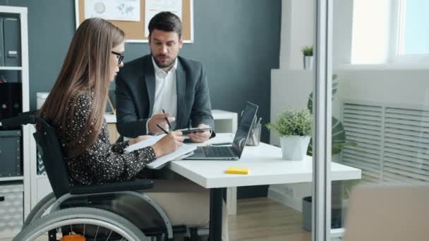 Empresarios mujer en silla de ruedas y hombre discutiendo el trabajo en el escritorio en la oficina — Vídeos de Stock