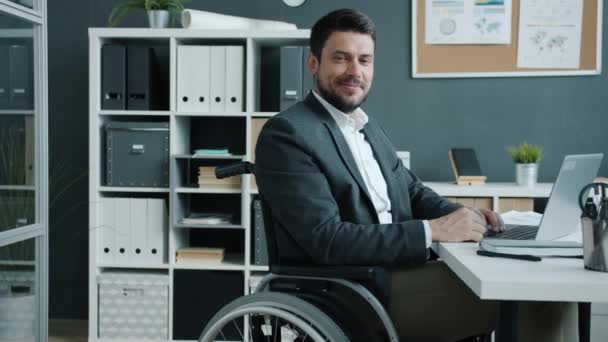 Portret van gehandicapte werknemer zittend in een rolstoel kijkend naar de camera en lachend op de werkplek — Stockvideo