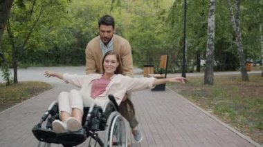 Tekerlekli sandalyedeki sakat adam ve engelli kadın, sonbahar günü parkta eğleniyor.