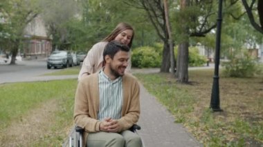 Şehir parkında tekerlekli sandalye iten genç bir kadınla konuşan engelli adam.