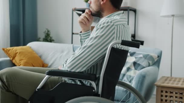 Vista lateral da pessoa com deficiência pensiva em cadeira de rodas pensando dentro de casa no apartamento — Vídeo de Stock