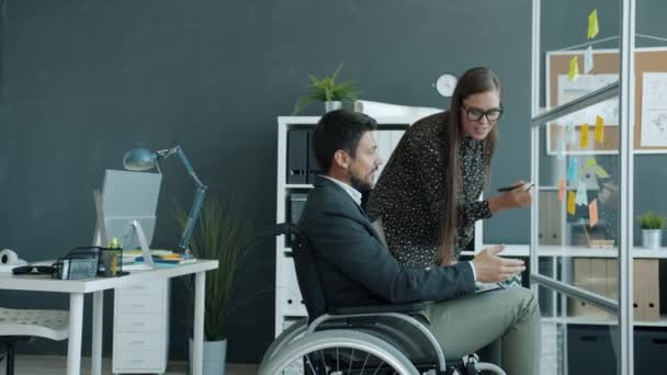 Dipendente disabile che lavora con appunti appiccicosi e parla con collega donna al chiuso in ufficio — Video Stock