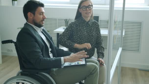 İş arkadaşları engelli erkek ve sağlıklı kadın ofiste yapışkan notlar hakkında bilgi tartışıyorlar. — Stok video