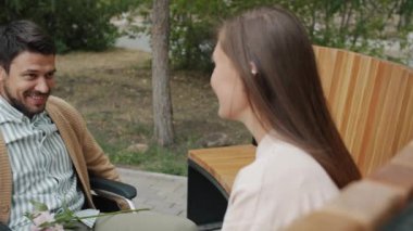 Tekerlekli sandalyeyi hareket ettiren engelli bir adam genç bir kadına el ele tutuşup gülüyor.