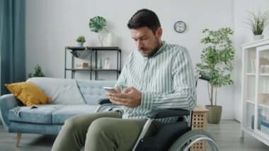 Tekerlekli sandalyede akıllı telefon kullanan genç bir adamın portresi evde gülümseyen güzel haberlerin tadını çıkarıyor.