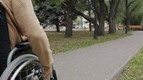 Dolly tiro de deficiente jovem montando cadeira de rodas na rua da cidade no dia de outono — Vídeo de Stock