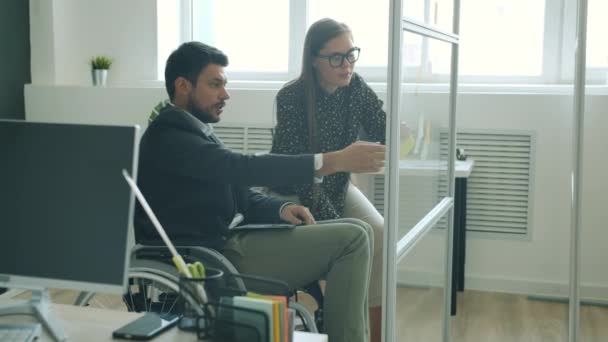 Disabled man working with sticky notes on glassboard and discussing project with female colleague — Stock Video