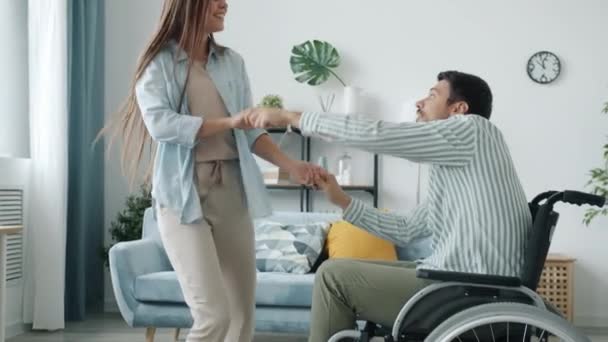 Νεαρός με ειδικές ανάγκες σε αναπηρικό καροτσάκι χορεύει με την ευτυχισμένη νεαρή κοπέλα στο σπίτι — Αρχείο Βίντεο