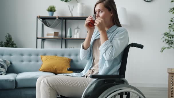 Movimiento lento de la joven solitaria en silla de ruedas sosteniendo la taza de té y bebiendo con cara seria — Vídeos de Stock