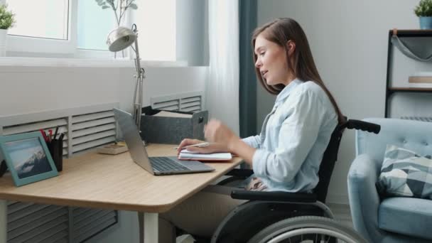 Mulher com deficiência ambiciosa fazendo videochamada com laptop conversando e escrevendo em apartamento — Vídeo de Stock