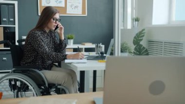 Tekerlekli sandalyedeki engelli iş kadınının ofiste cep telefonuyla konuşması