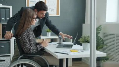 Tekerlekli sandalyede çalışan engelli bir ofis çalışanı, erkek meslektaşıyla bilgisayar ekranına bakıyor.