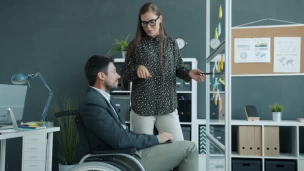 Joyful businesspeople disabled man and healthy woman working with colorful sticky notes on glass board — Stock Video