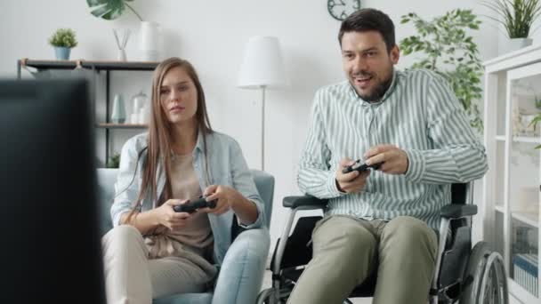 Hombre discapacitado jugando videojuego con novia ganando bailando en silla de ruedas en casa — Vídeos de Stock