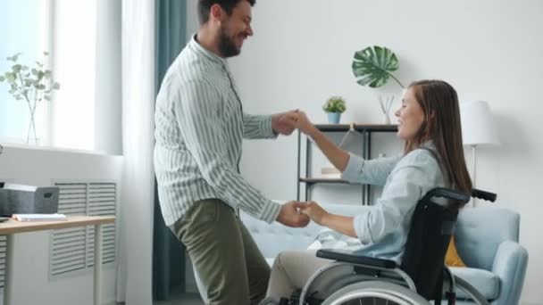 車椅子の女性とハンサムな男がアパートで楽しんで踊っている — ストック動画