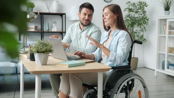 Familia feliz mujer discapacitada y hombre hablando y mirando la pantalla del ordenador portátil sonriendo en el escritorio en casa — Vídeos de Stock