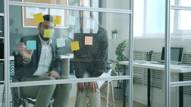 Slow motion of creative business people disabled man and young woman discussing information on sticky notes — Stock Video
