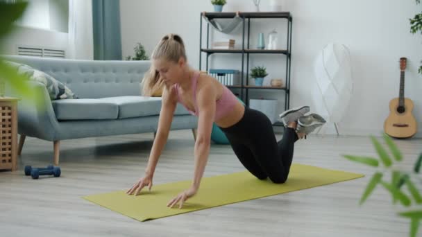 Trage beweging van actieve meisje in sportkleding uit te werken thuis op yoga mat genieten van de praktijk — Stockvideo