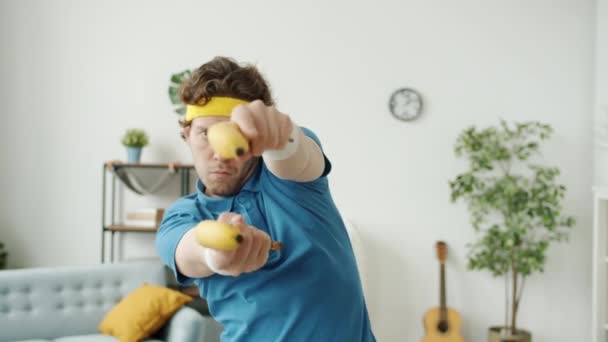 Rallentatore di uomo sciocco che spara con pistole a banana guardando la fotocamera al chiuso in appartamento — Video Stock